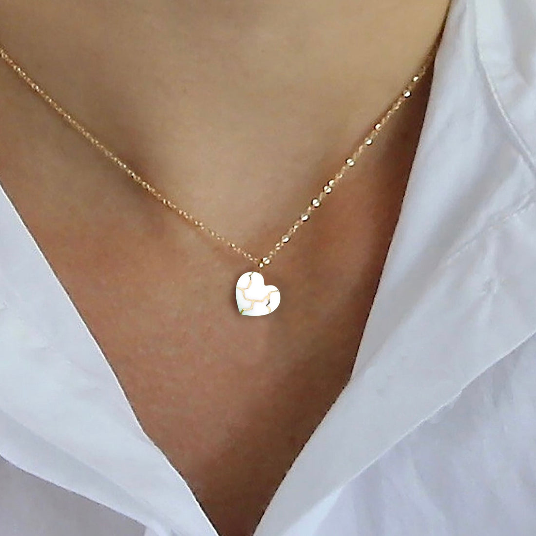 Gold Kintsugi necklace featuring a heart-shaped pendant of white porcelain with gold accents, symbolizing a mended broken heart and the beauty of imperfections. Gold Kintsugi necklace showcasing a heart-shaped pendant in white porcelain with gold accents. Inspired by the historical Japanese art of Kintsugi, this piece symbolizes the beauty in mending and embracing imperfections. Kintsukuroi necklace with 24k gold